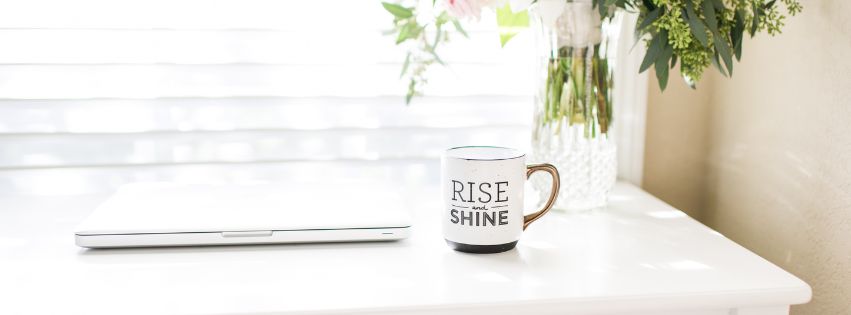 Grafika do artykułu o tym czemu warto stworzyć swój pierwszy produkt cyfrowy. Na zdjęciu biurko, laptop, kubek i kwiaty w wazonie.