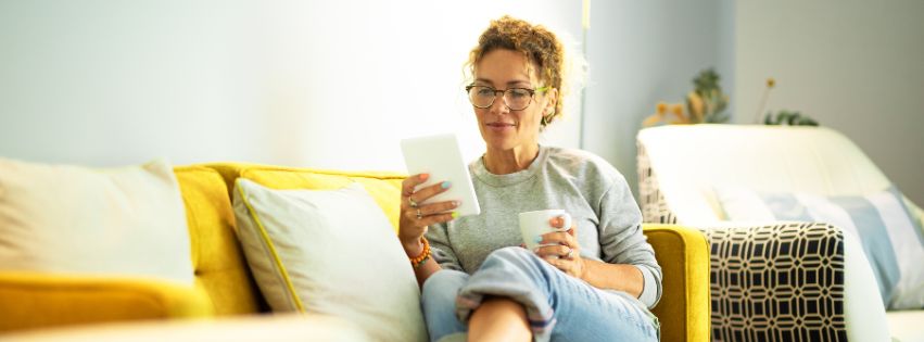 Kobieta siedząca na kanapie, przegląda e-book na tablecie i trzyma kubek, symbolizując korzystanie z lead magnetu w formie e-booka.