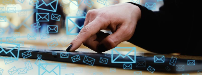 Osoba pisząca na tablecie, otoczona ikonami wiadomości e-mail, symbolizującymi komunikację mailową i newslettery.